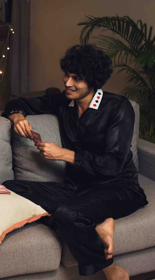 Relaxed man in stylish Play-Boy pyjama suit playing cards on sofa.