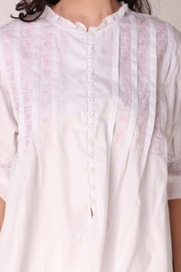 White pyjama suit with delicate pink embroidery and button details.