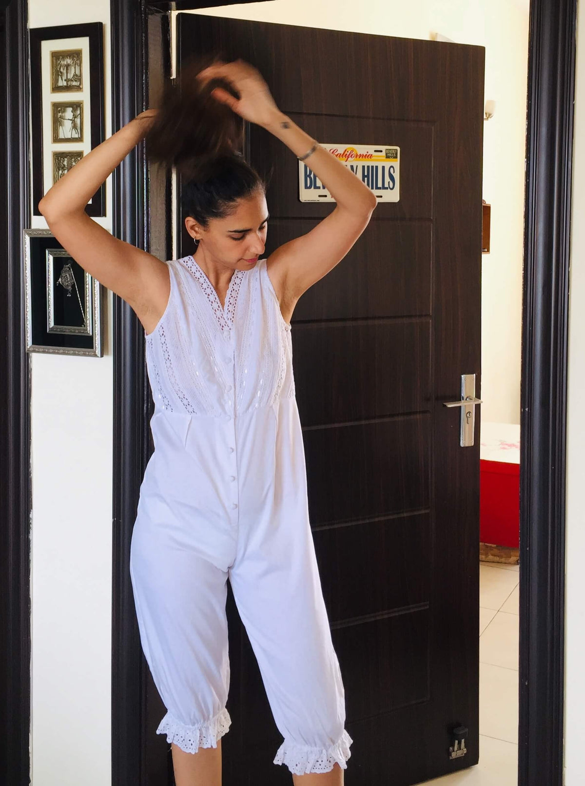 White Enola romper on a woman adjusting her hair indoors.