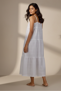 Woman wearing a white dress standing against a beige wall with soft shadows.