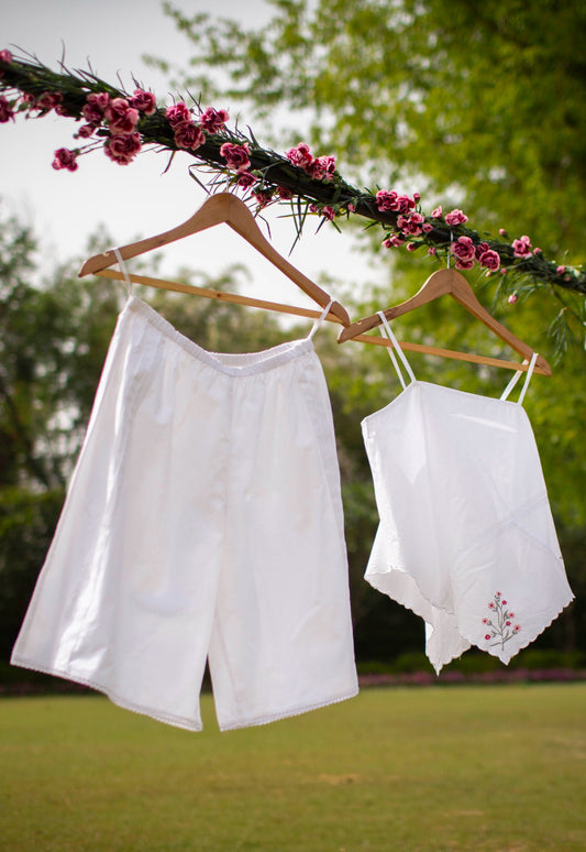 White shorts and cami set displayed outdoors with flowers.